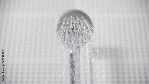 Close-up of turning on and off shower head in bathroom, white tiles with black pattern on the walls, focus on water sprays out and flowing slowly, falling drops photo
