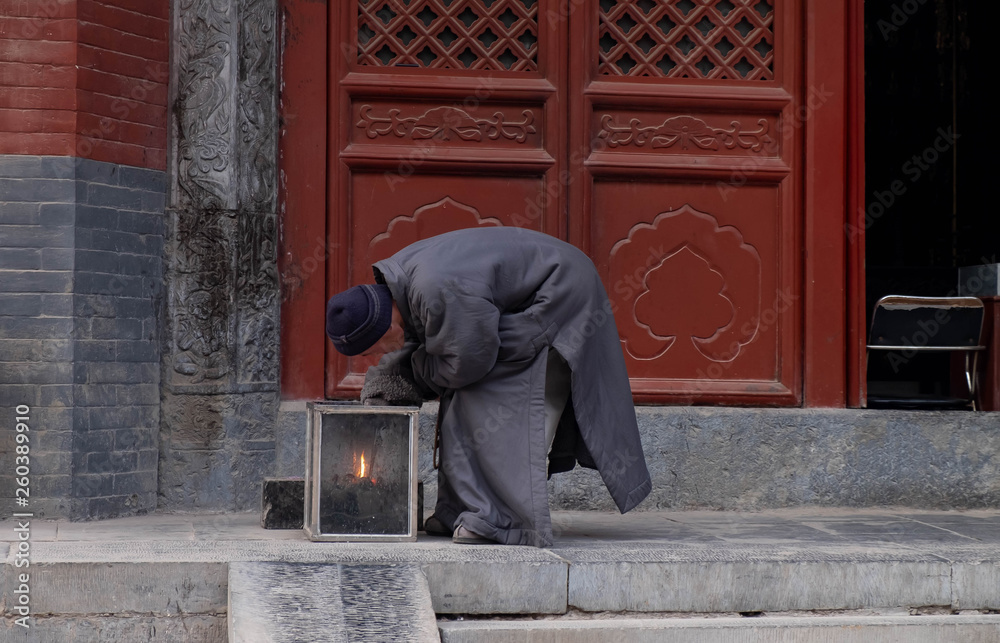 The Unspecific chinese monk lights a candle for buddhist prayers