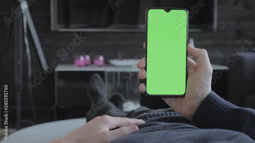 Green screen - Man at home lying on a couch looking at a smartphone.