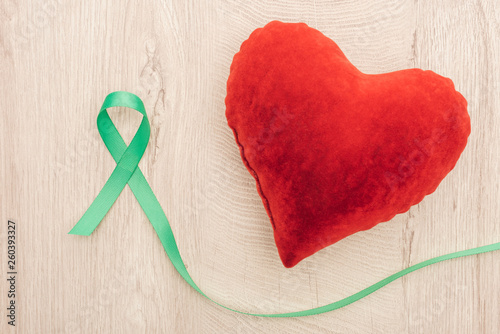 top view of bright toy heart and green ribbon on wooden background