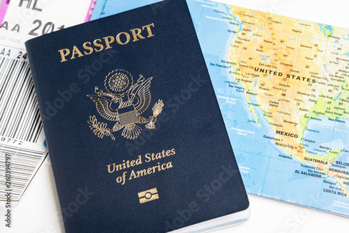 The iconic dark blue cover of an American passport with gold stamp set with a folded world map and portion of a luggage tag artistically set on a plain white background.