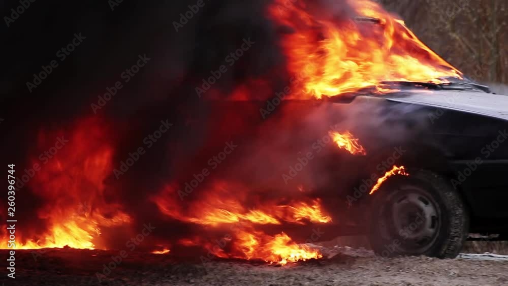 Huge red flame of fire with massive matt black smoke totally burns rusty dirty old dark dusty car which is left on deserted grey road at some suburb area on cold cloudy winter day. Huge red flame of fire with massive matt black smoke totally burns rusty dirty old dark dusty car which is left on deserted grey road at some suburb area on cold cloudy winter day.