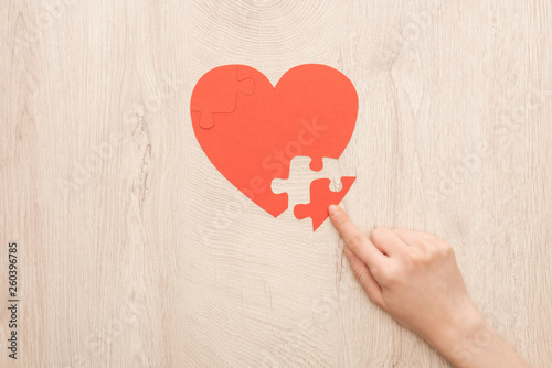 cropped view of woman pointing with finger to puzzle of heart