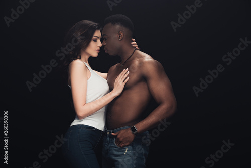 beautiful seductive woman embracing shirtless african american man isolated on black with copy space