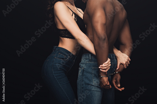 partial view of sexy woman hugging shirtless african american man in handcuffs isolated on black