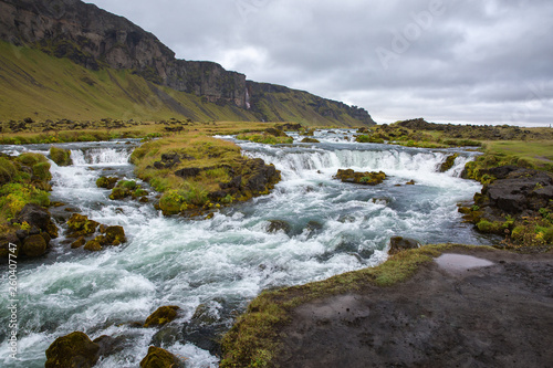 Stormy mountain river with rapids and green islets in the middle. Against the backdrop of mountains and a leaden sky