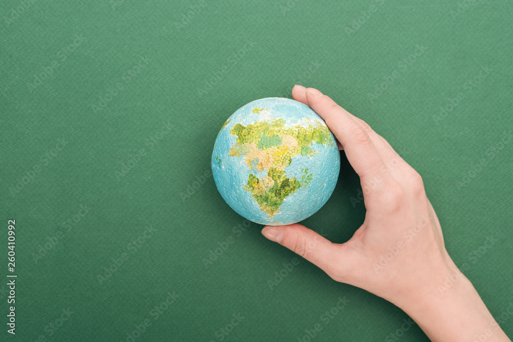 partial view of woman holding toy earth on green background with copy space partial view of woman holding toy earth on green background with copy space