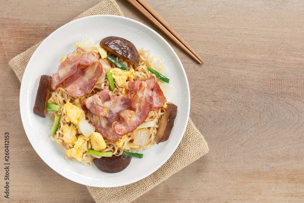 top view of stir fried instant noodle with bacon and vegetable in a ceramic dish on wooden table. asian homemade stlye food concept. top view of stir fried instant noodle with bacon and vegetable in a ceramic dish on wooden table. asian homemade stlye food concept.