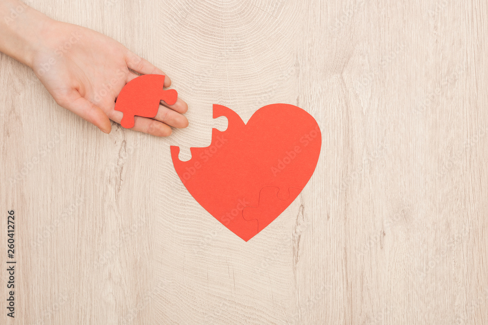 partial view of woman holding puzzle of heart on wooden background partial view of woman holding puzzle of heart on wooden background