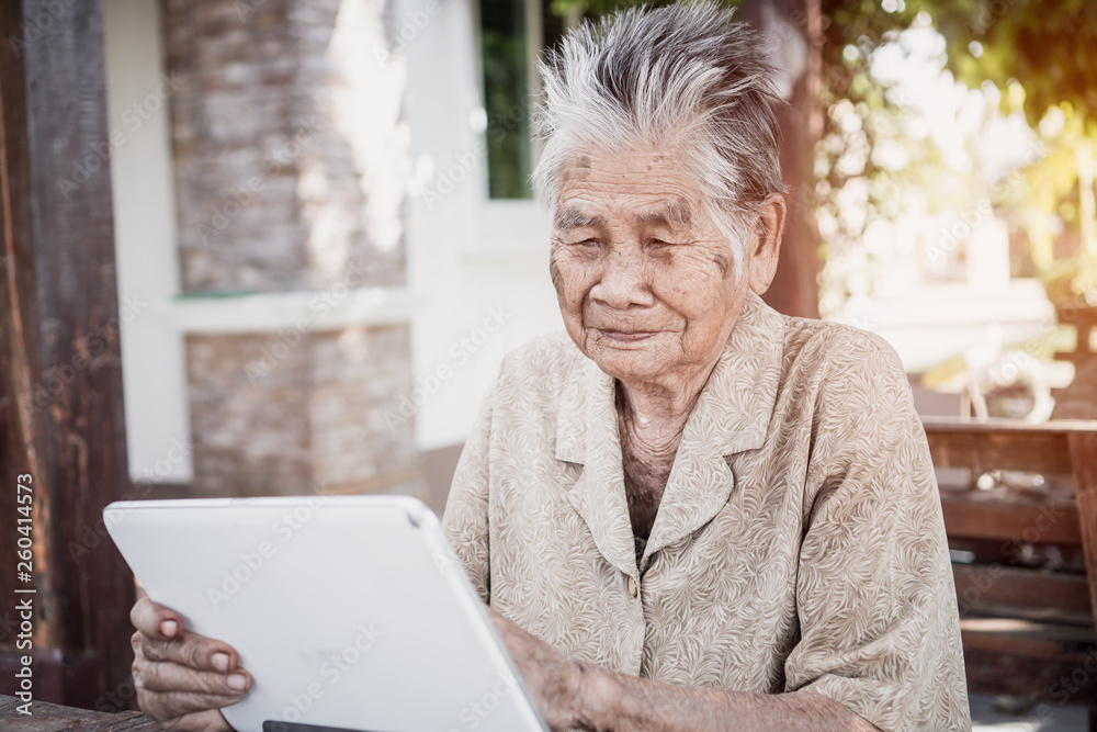 Happy Asian old woman / grandmother smiling and using tablet pointing finger on touching screen for typing chating sms message to Grandchildren Happy Asian old woman / grandmother smiling and using tablet pointing finger on touching screen for typing chating sms message to Grandchildren