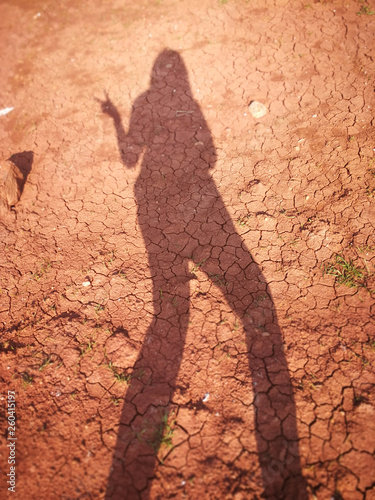 The shadow of the woman on the dry orange clay surface of the ground