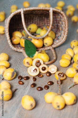 The vertical photo of a basket with chinese fruit, loquat, over wooden background photo
