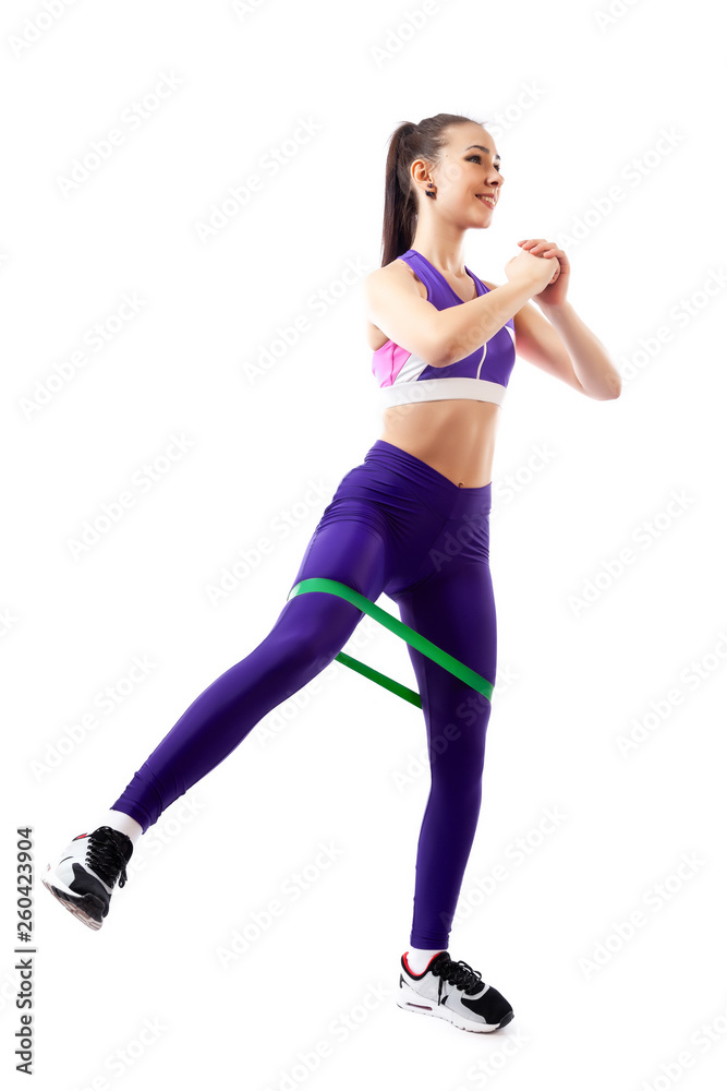 Sporty woman does exercises on legs, makes lunges with sport fitness rubber bands on white background. Photo of muscular woman in sportswear on white background. Strength and motivation. Sporty woman does exercises on legs, makes lunges with sport fitness rubber bands on white background. Photo of muscular woman in sportswear on white background. Strength and motivation.