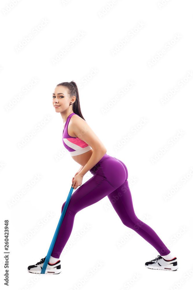 Sporty woman does exercises on legs, makes lunges with sport fitness rubber bands on white background. Photo of muscular woman in sportswear on white background. Strength and motivation. Sporty woman does exercises on legs, makes lunges with sport fitness rubber bands on white background. Photo of muscular woman in sportswear on white background. Strength and motivation.