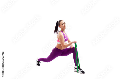 Beautiful young woman doing lunge exercisewith sport fitness rubber bands in fitness gym isolated over white background. Fit girl living an active lifestyle