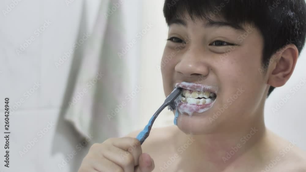 Little asian boy brushing his teeth in bathroom in front of mirror, oral hygiene. Young child brushes teeth before going to bed.