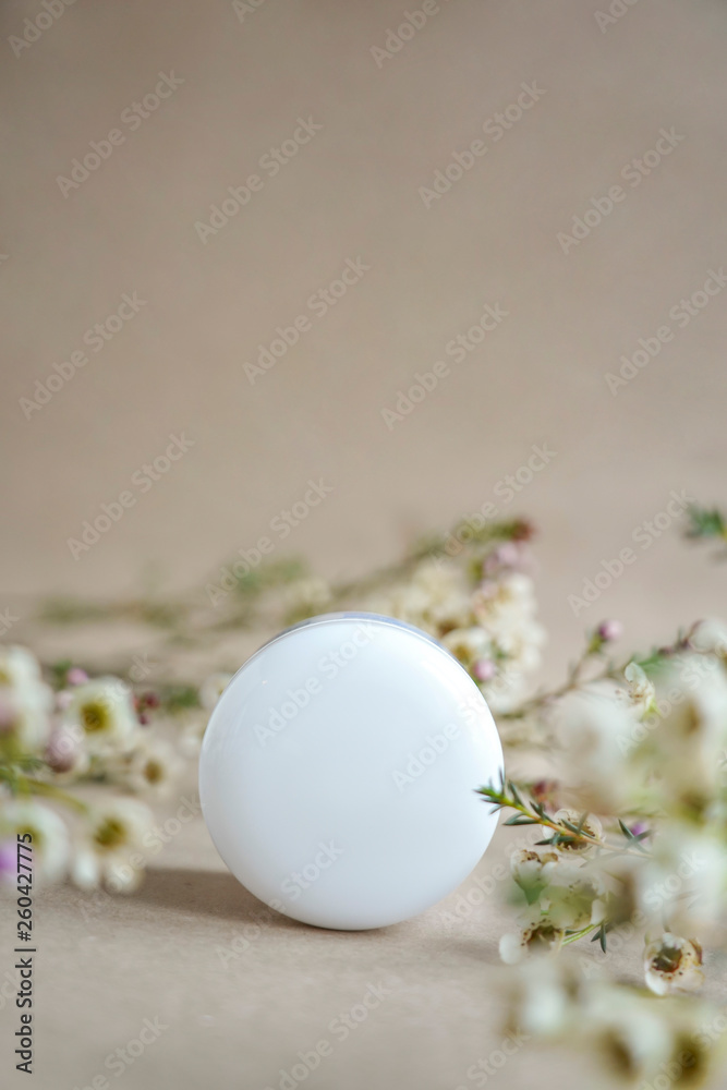 White  round cosmetic jar on a beige background decorated with white flowers