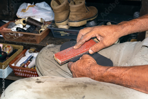 Shoemaker polishes the sole of old sneakers in the street workshop. Close-up