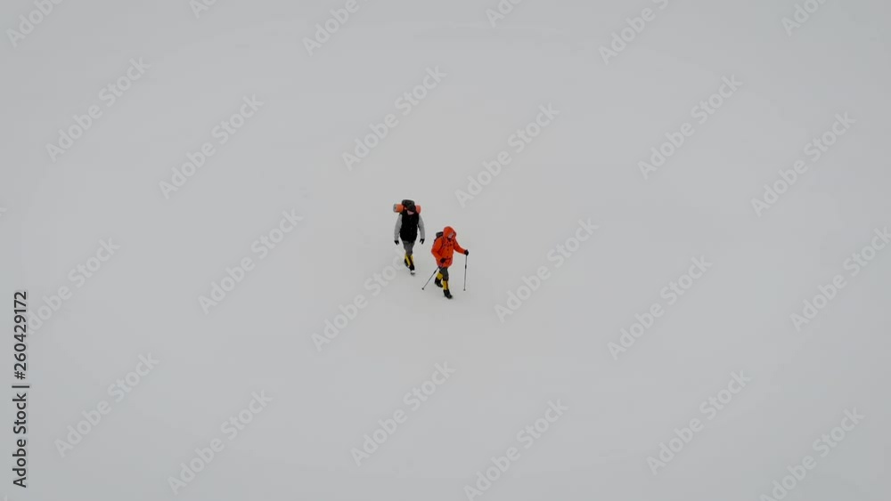 two extreme travelers are strolling over snow field in winter, aerial view, drone is flying over them two extreme travelers are strolling over snow field in winter, aerial view, drone is flying over them