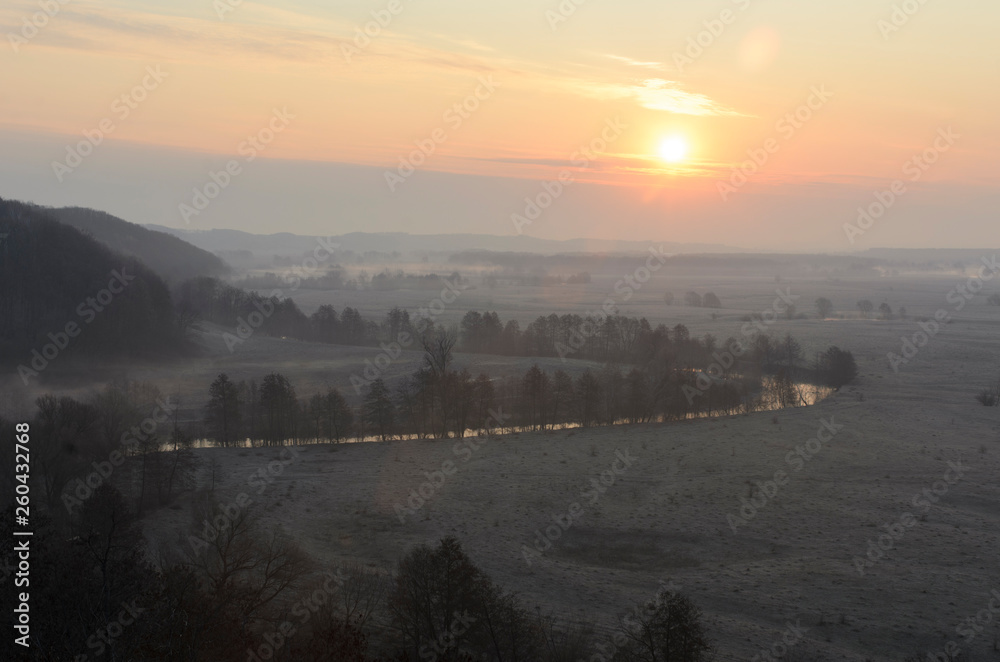 Landscape of amazing spring nature in early foggy morning on sunrise. Trees on river bank in mist on warm sunlight background. Perfect scene of Wild nature at dawn. Colorful sky over forest and river Landscape of amazing spring nature in early foggy morning on sunrise. Trees on river bank in mist on warm sunlight background. Perfect scene of Wild nature at dawn. Colorful sky over forest and river