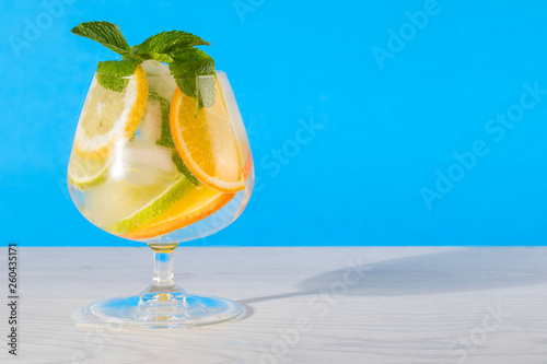 Refreshing cocktail with orange lemon lime mint and ice on a bright blue background