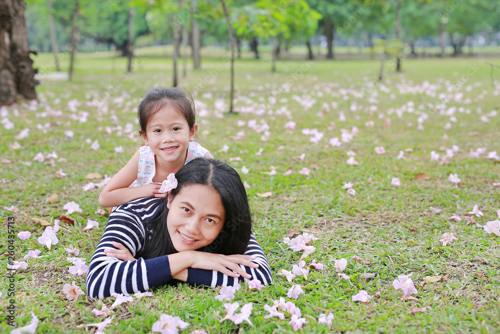 Happy Asian mother and her daughter cuddle lying on green field with fully fall pink flower in the garden outdoor. Happy Asian mother and her daughter cuddle lying on green field with fully fall pink flower in the garden outdoor.