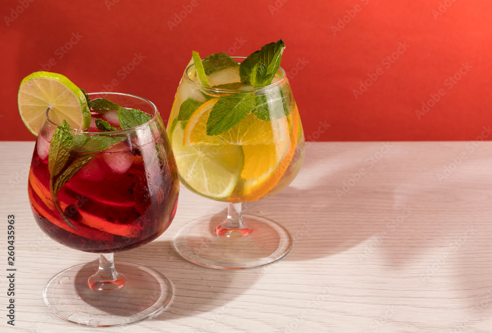 Two refreshing cocktails with orange lemon lime mint and ice on a bright coral background Two refreshing cocktails with orange lemon lime mint and ice on a bright coral background
