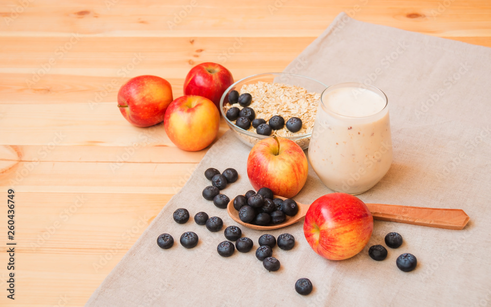 Glass of yogurt, apples, bilberries and oat flakes in bowl on wooden table. Glass of yogurt, apples, bilberries and oat flakes in bowl on wooden table.