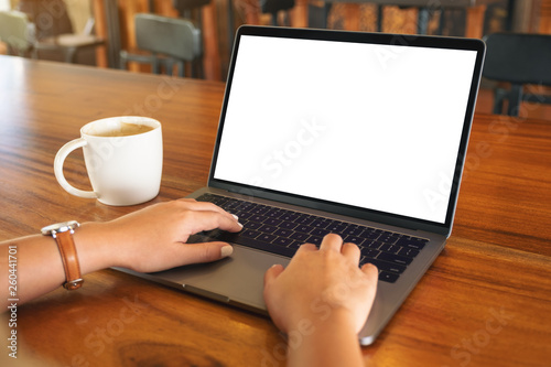 Mockup image of a woman using and typing on laptop with blank white screen and coffee cup on wooden table