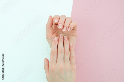 Stylish trendy female classic french manicure. Beautiful young woman s hands on pink and white background.