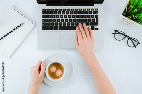 Female hands working on modern laptop and holds cup of coffee. Office desktop on white background