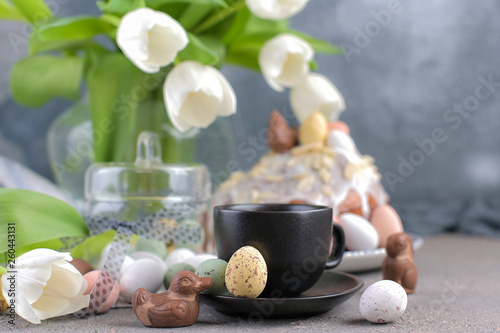 Fragrant cup of coffee and Easter orthodox sweet bread, kulich and colorful quail eggs with willow branches. Holidays breakfast concept with copy space. Set for the holiday and a bouquet of tulips.