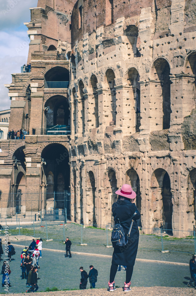 Woman traveler,dressed in black with pink hat looking at Colosseum.