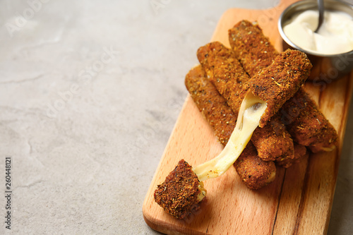 Wooden board with tasty mozzarella sticks and sauce on grey table photo