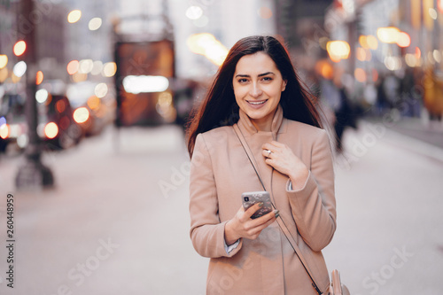 Beautiful girl in a park. Stylish brunette in a brown jacket. Lady with a phone