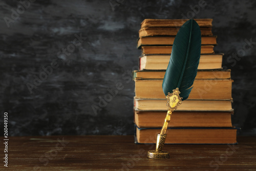 фотографія Old feather quill ink pen with inkwell and old books over wooden desk infront of black wall background