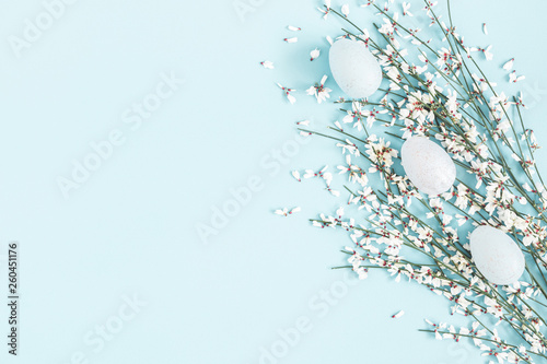 Easter composition. Easter eggs, white flowers on pastel blue background. Flat lay, top view, copy space