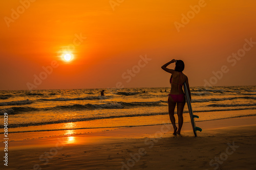 silhouette young asian tourist in bikini with holding hands surfboard on the beach and the sunset  seascape background