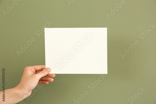Female hand with blank invitation card on color background