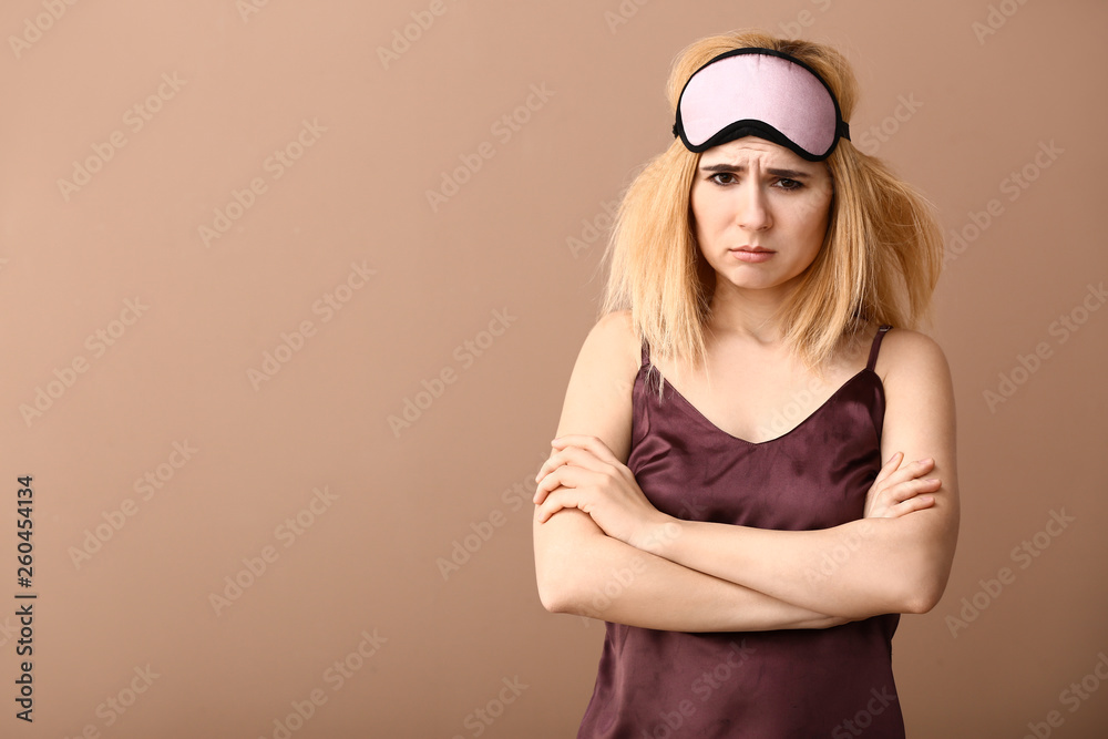 Displeased woman with sleep mask on color background