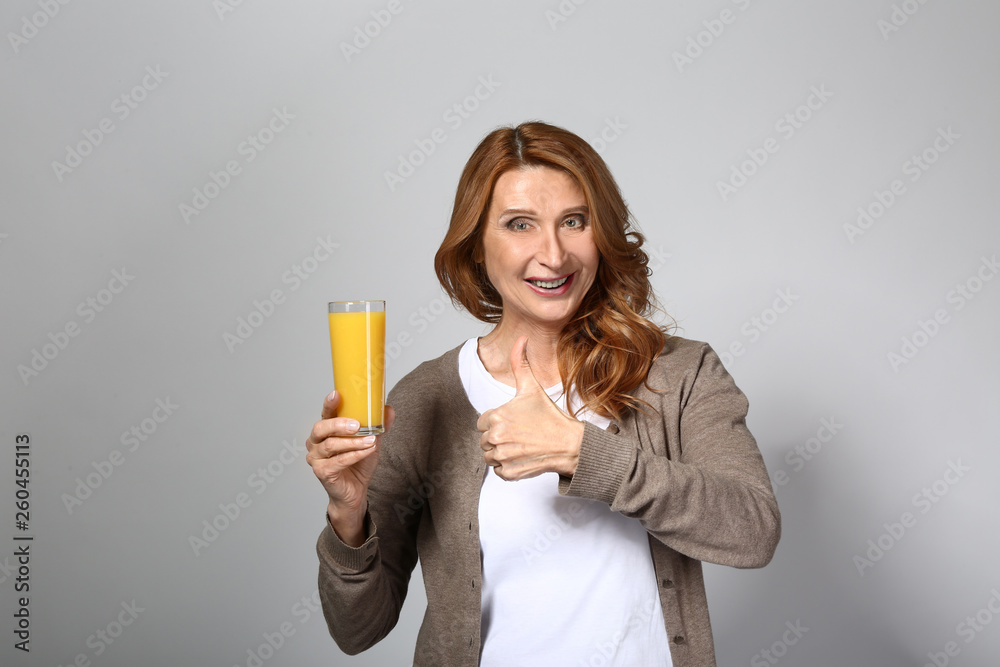 Mature woman with glass of fresh juice on grey background Mature woman with glass of fresh juice on grey background