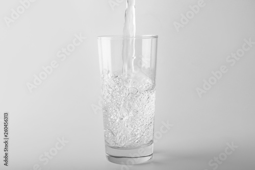 Pouring of water into glass on light background