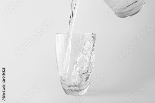 Pouring of water into glass on light background
