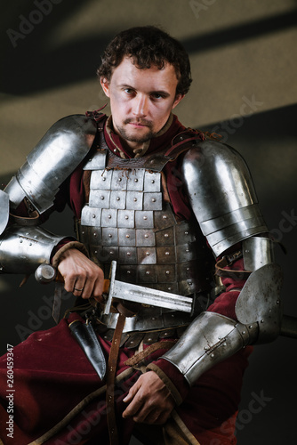 Medieval man knight in armor and weapon on dark background. Portrait of the knight