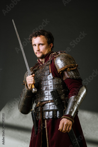 Medieval man knight in armor and weapon on dark background. Portrait of the knight