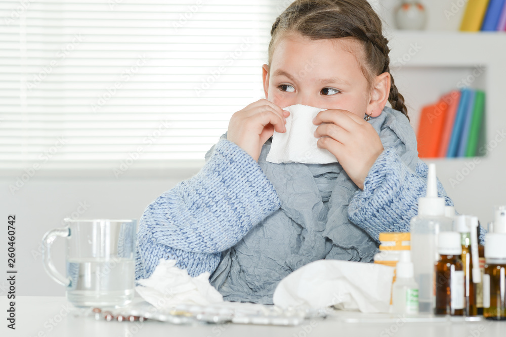 Close up portrait of ill little girl in blue sweater sitting at table with medicines Close up portrait of ill little girl in blue sweater sitting at table with medicines