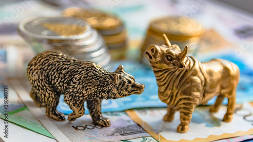 The bronze bull and bear figurines are arranged with paper money and metal coins. Blur background. Symbol and concept of trading on the stock exchange.