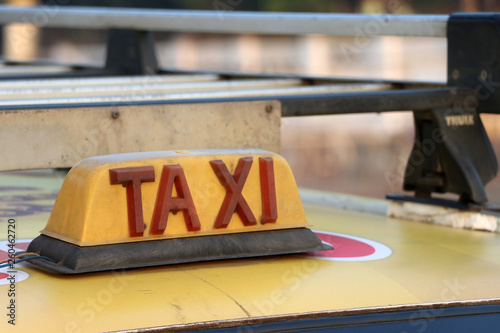 Taxi light sign or cab sign in drab yellow color with red text on the car roof.