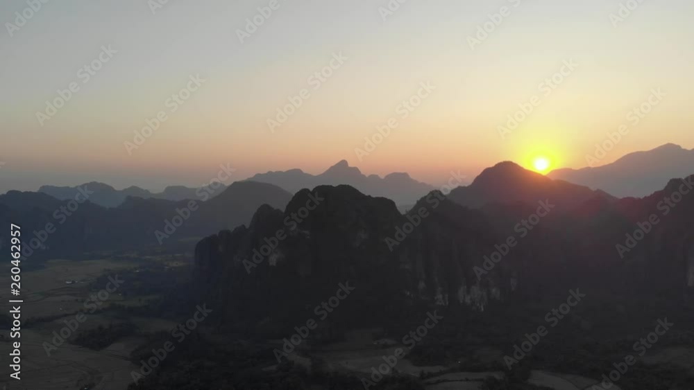 Aerial: Vang Vieng backpacker travel destination in Laos, Asia. Sunset scenic cliffs rock pinnacles rice paddies valley stunning landscape. Native cinelike D-log color profile
