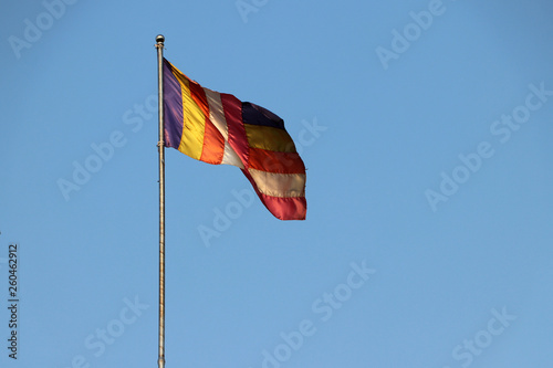 Fabric Buddhist flag blown by wind on the flagpole with blue sky background.